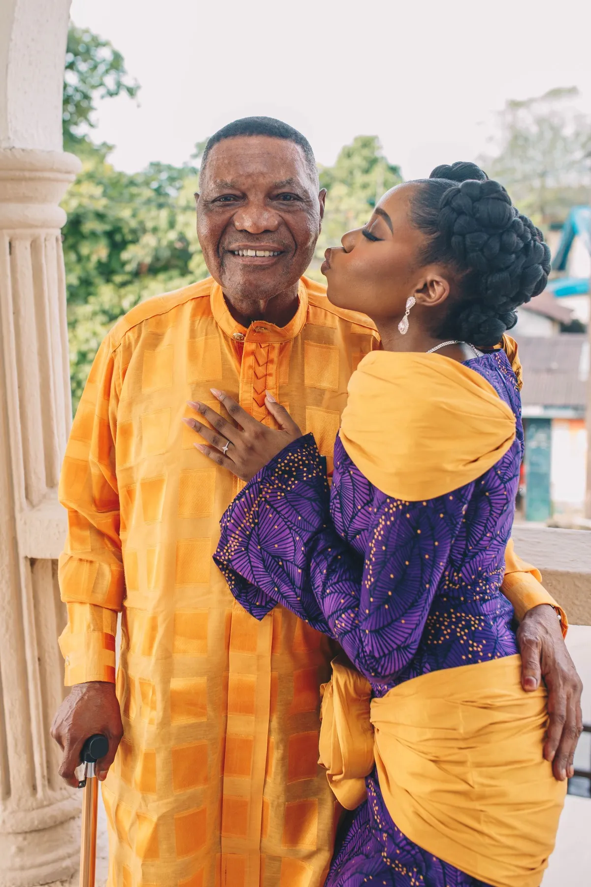 adeilé kissing the cheek of an older man in gold