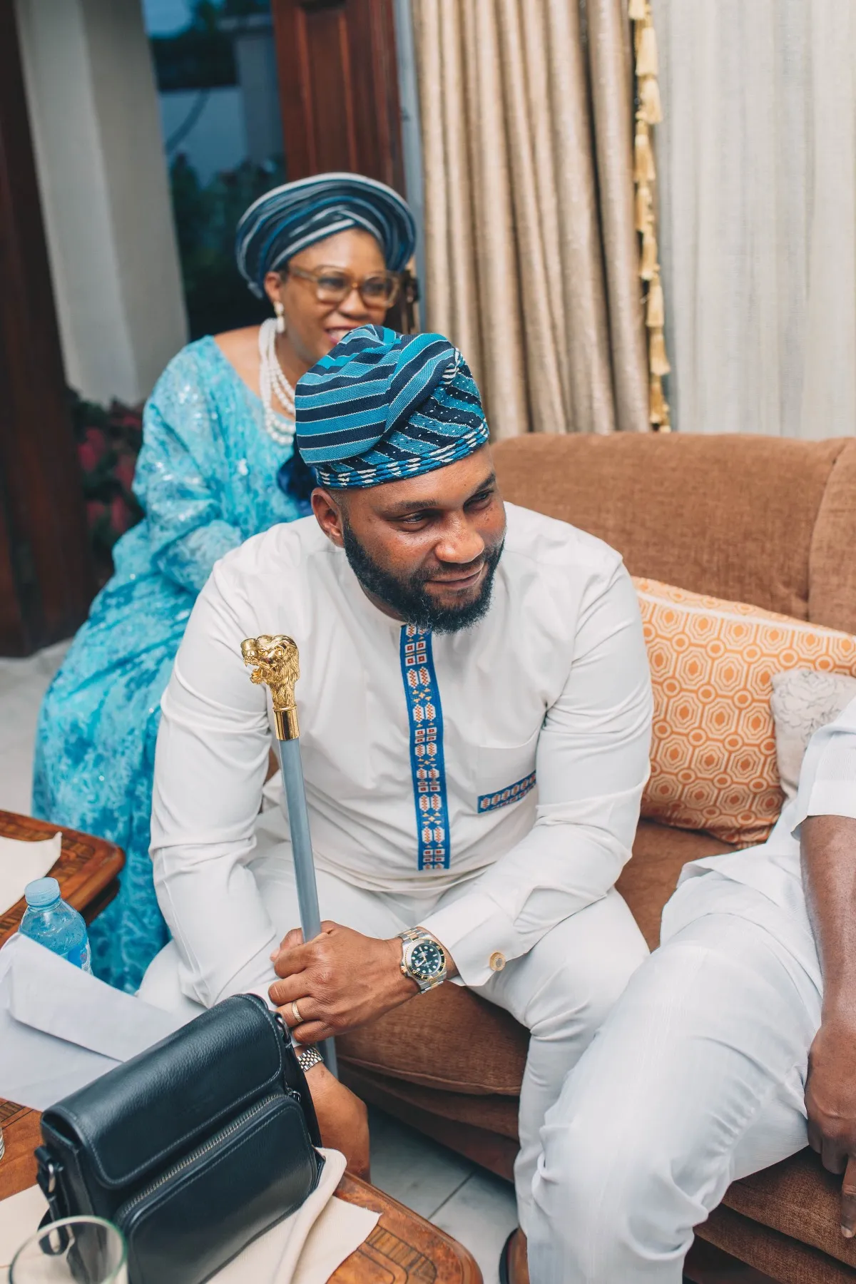 a guest in white and blue cap seated beside a woman in blue gele